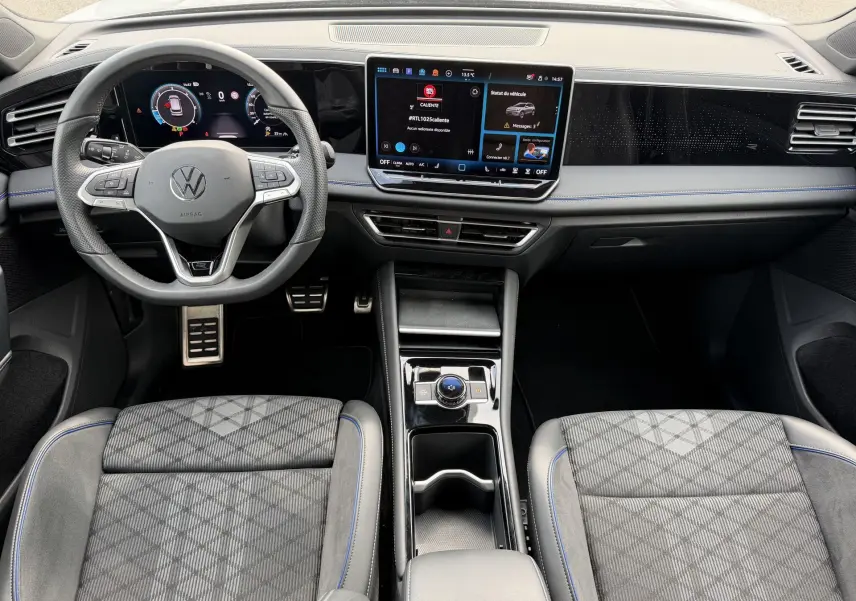 Vue intérieure avant du Volkswagen Tiguan 2025 gris, volant multifonction, écran tactile central et sièges sport à surpiqûres bleues.
