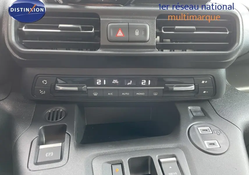 Vue rapprochée de la console centrale du Citroën Berlingo noir, montrant les commandes de climatisation et le frein à main électrique.