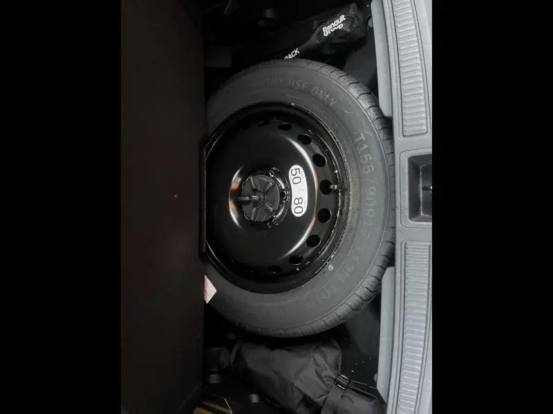 Roue de secours compacte noire vue dans le coffre d'un Renault Austral blanc 2023, entourée d'accessoires de rangement.