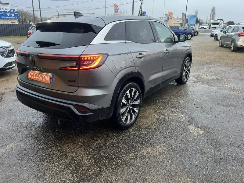 Renault Austral gris métallisé vu en 3/4 arrière droit sur parking, feux arrière LED allumés et jantes alliage.