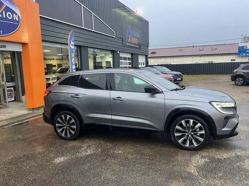 Vue de profil côté droit d'un Renault Austral gris métallisé garé devant un garage avec jantes alliage noires et chromées.