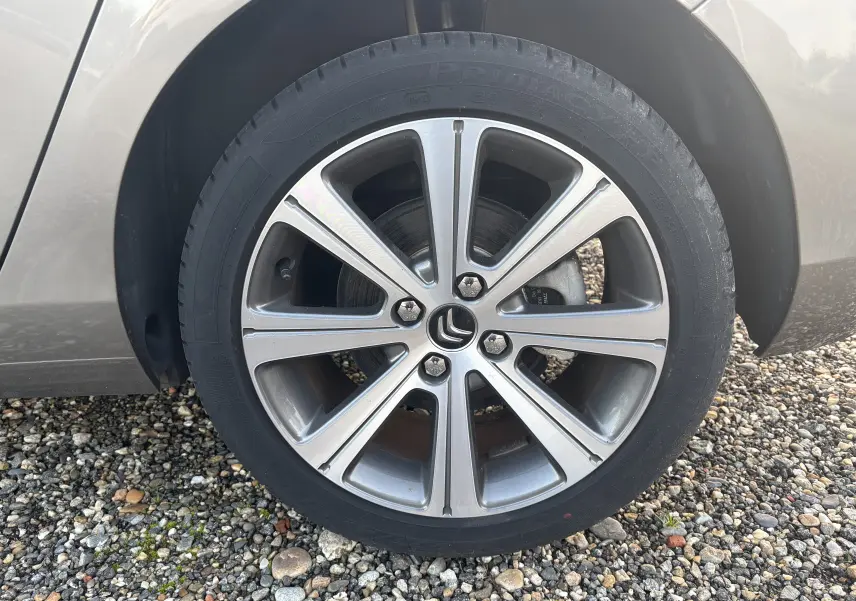 Gros plan sur la roue avant gauche d'une Citroën C4 gris clair, jante alliage à cinq doubles branches.