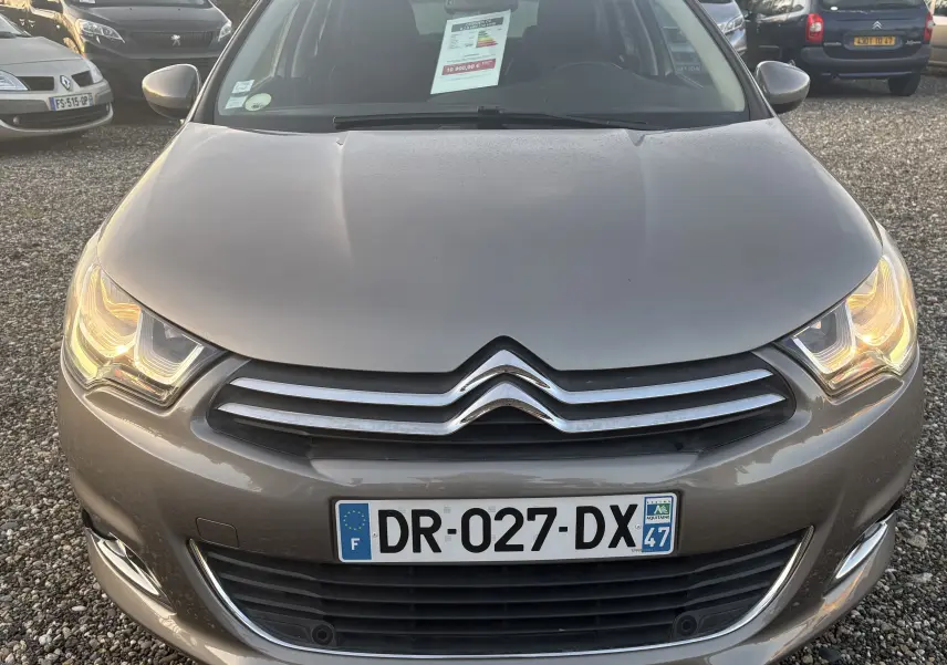Vue frontale d'une Citroën C4 II gris métallisé avec phares allumés et plaque d'immatriculation française visible.