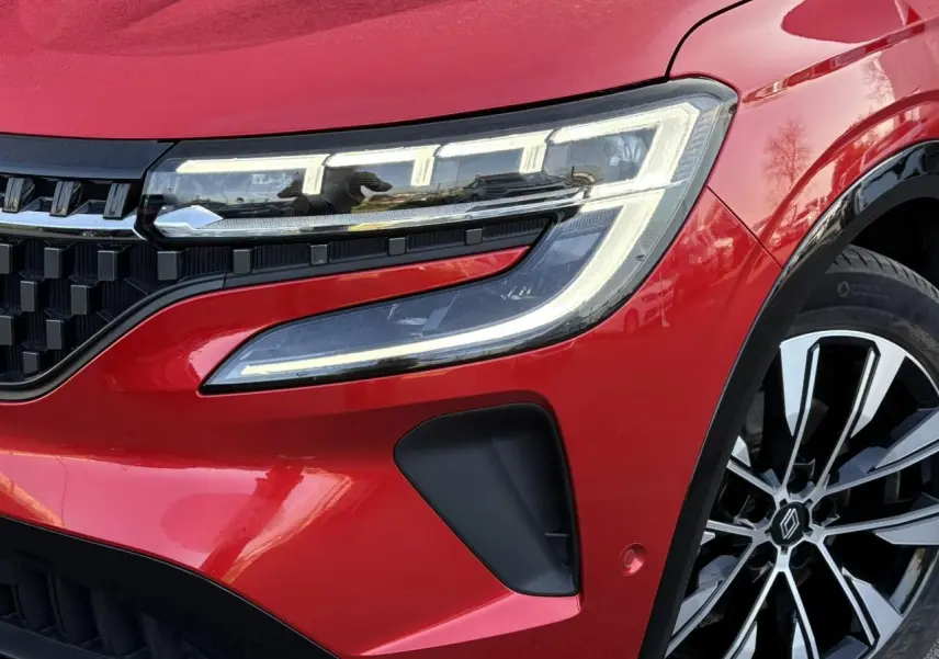 Gros plan sur le phare avant droit et la jante alliage noire et argent du Renault Austral Rouge Flamme 2024.