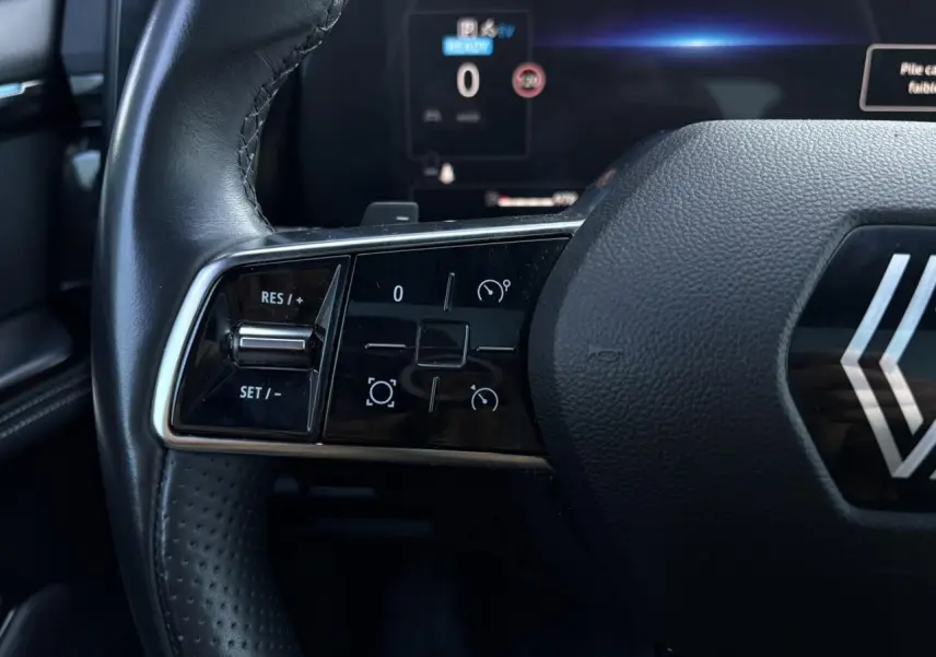 Gros plan sur les commandes à gauche du volant cuir du Renault Austral E-Tech 2024, affichage numérique en arrière-plan.