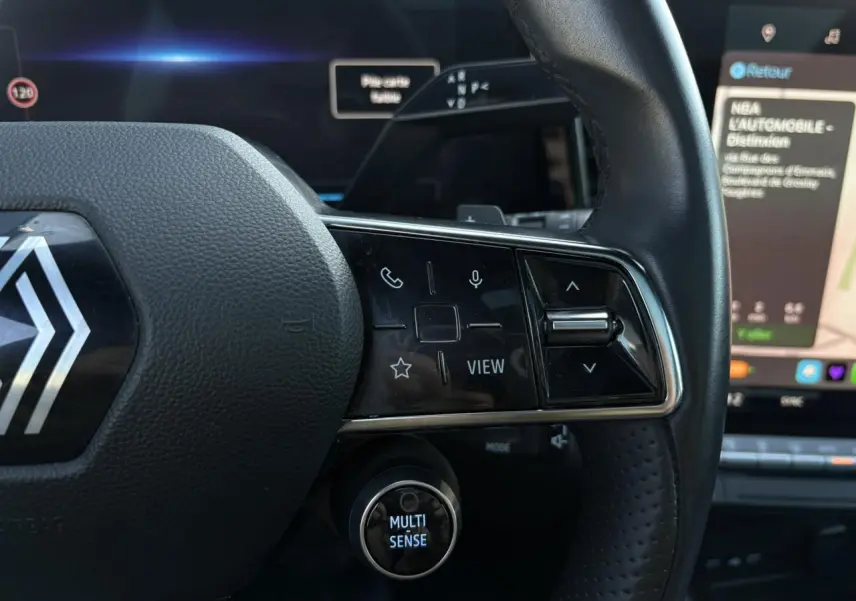 Gros plan sur le volant cuir du Renault Austral rouge, avec commandes multifonctions et bouton Multi-Sense éclairé.