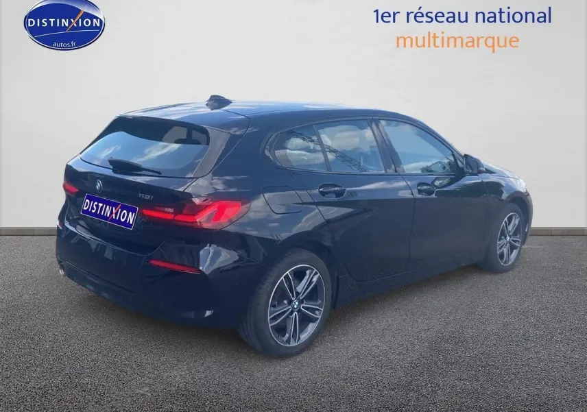 BMW Série 1 noire vue 3/4 arrière droit, avec jantes alliage et feux arrière LED allumés.