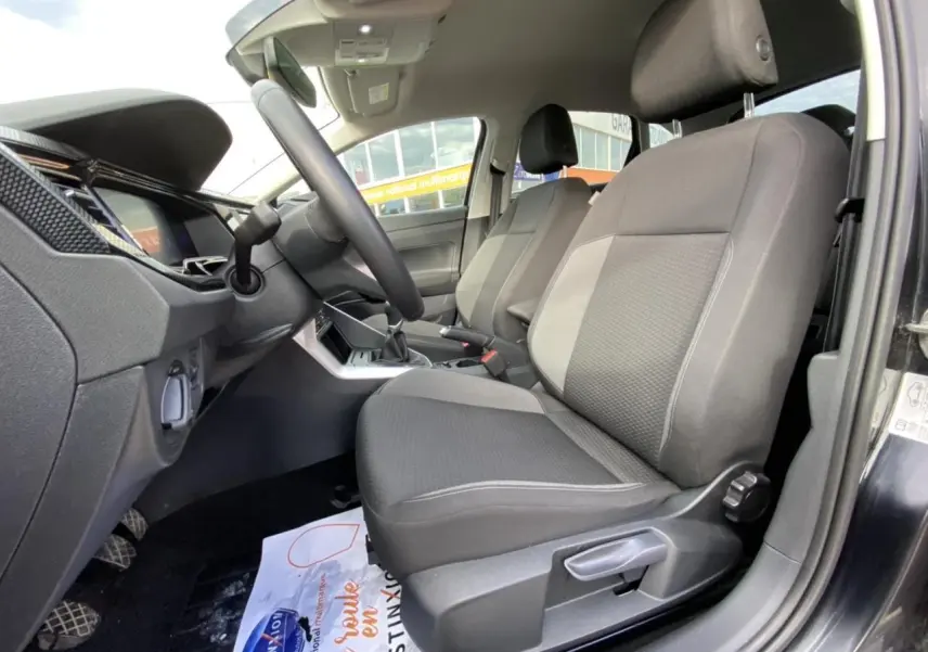 Intérieur côté conducteur du Volkswagen Taigo noir intense 2022, sièges tissu gris et console centrale visible.