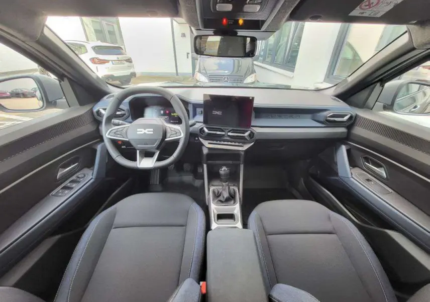 Vue intérieure avant du Dacia Duster TCE 130 4x2 Journey 2025, montrant le tableau de bord moderne et la boîte manuelle.