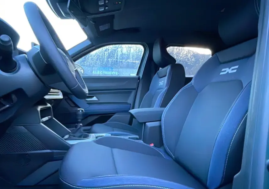 Vue intérieure côté conducteur du Dacia Duster TCE 130 4x2 Journey 2025 avec sièges noirs et logo DC brodé.