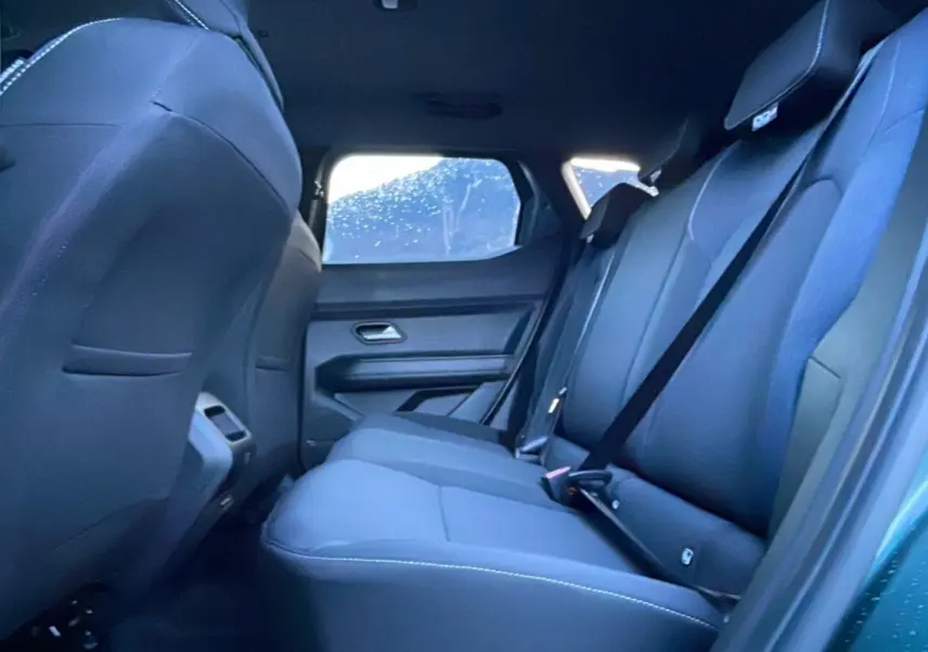 Vue intérieure arrière côté droit du Dacia Duster 2025 vert cèdre, montrant les sièges arrière en tissu sombre.