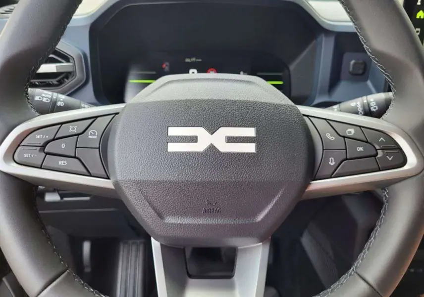 Gros plan sur le volant multifonction du Dacia Duster 2025, avec commandes intégrées et logo central distinctif.