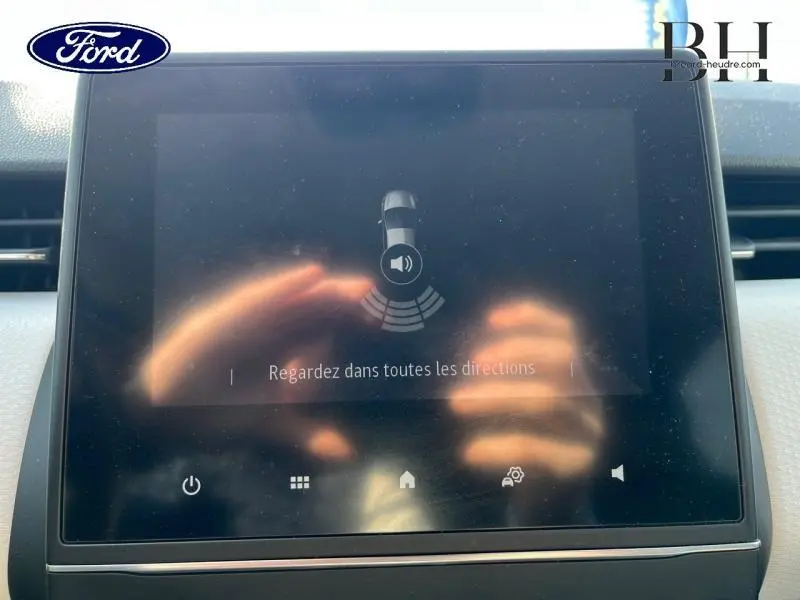 Vue rapprochée de l'écran tactile central de la Renault Clio gris platine 2023, affichant une alerte de stationnement.