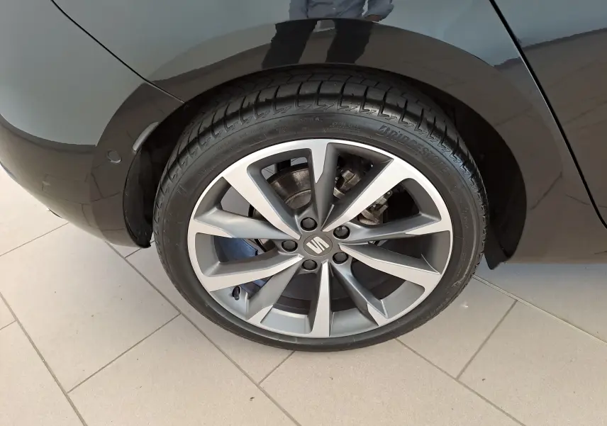 Gros plan sur la roue arrière droite d'une SEAT LEON 1.5 eTSI Hybrid 2024 en noir minuit avec jante alliage distinctive.