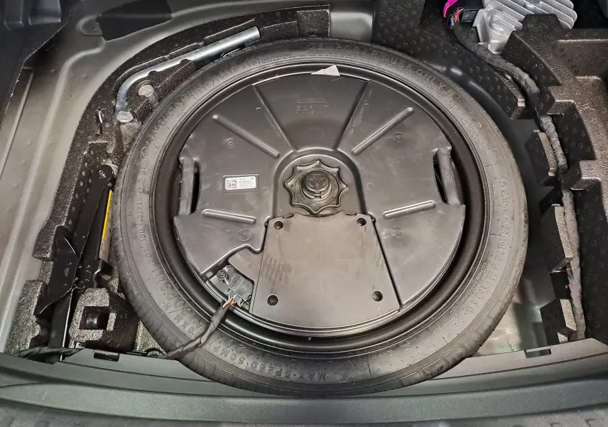 Vue plongeante sur la roue de secours et le cric dans le coffre du SEAT LEON 1.5 eTSI Hybrid 2024 noir minuit.