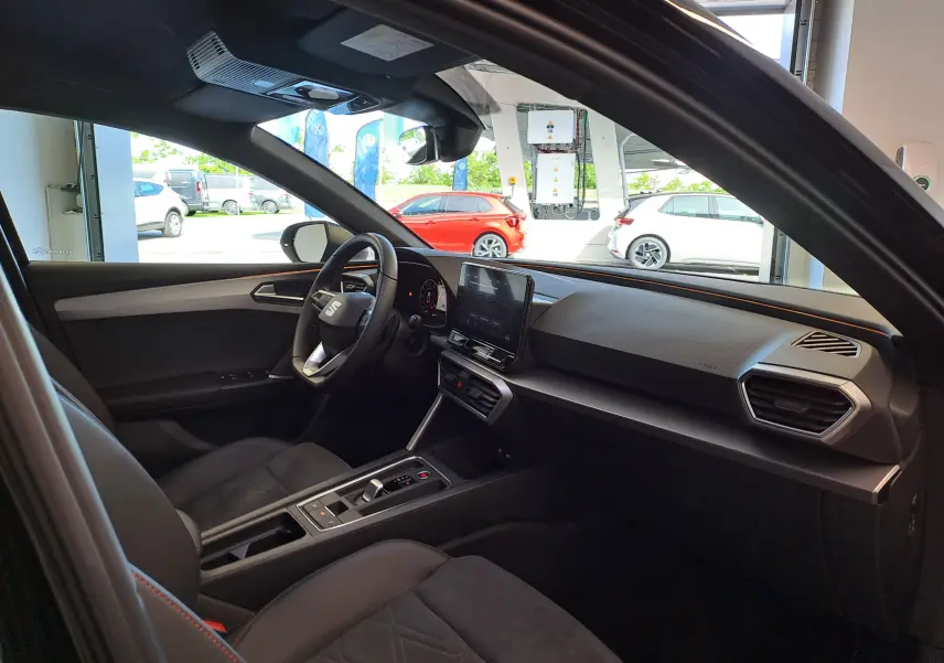 Intérieur de la SEAT LEON 1.5 eTSI Hybrid 2024 vu côté conducteur, avec tableau de bord moderne et sièges noirs.