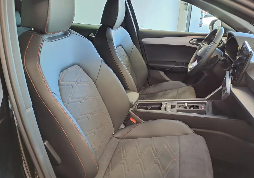 Intérieur de la SEAT LEON 1.5 eTSI Hybrid 2024, vue côté gauche, sièges noirs avec surpiqûres rouges et console centrale moderne.