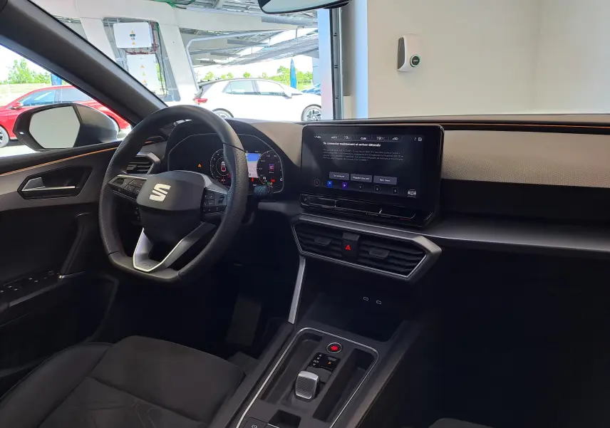 Intérieur de la SEAT LEON 1.5 eTSI Hybrid 2024 en noir, vue côté conducteur avec tableau de bord digital et écran tactile central.