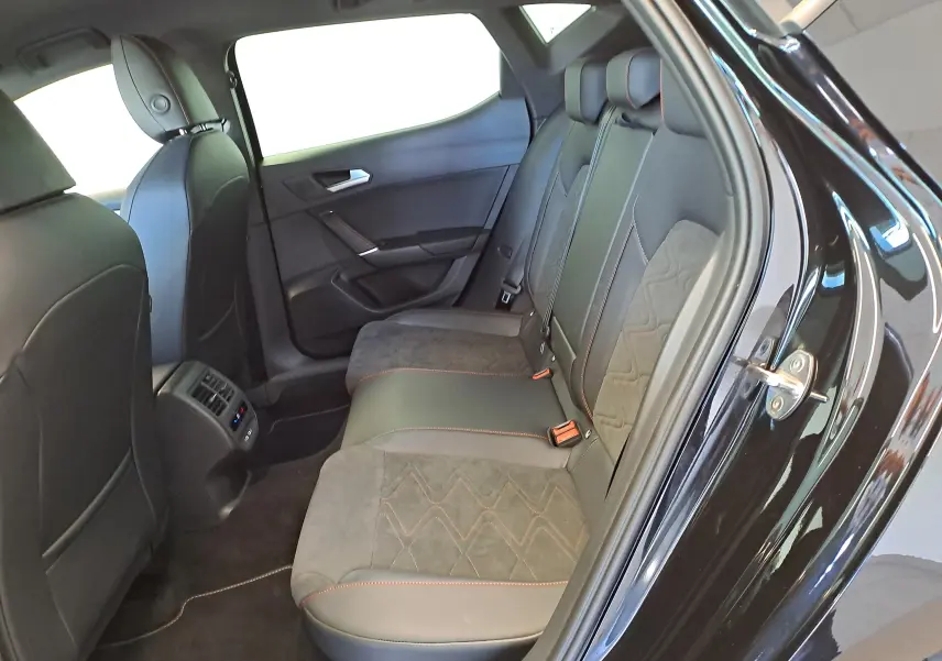 Vue intérieure côté arrière droit de la SEAT LEON 1.5 eTSI Hybrid 2024 noir minuit avec sièges en cuir et alcantara.