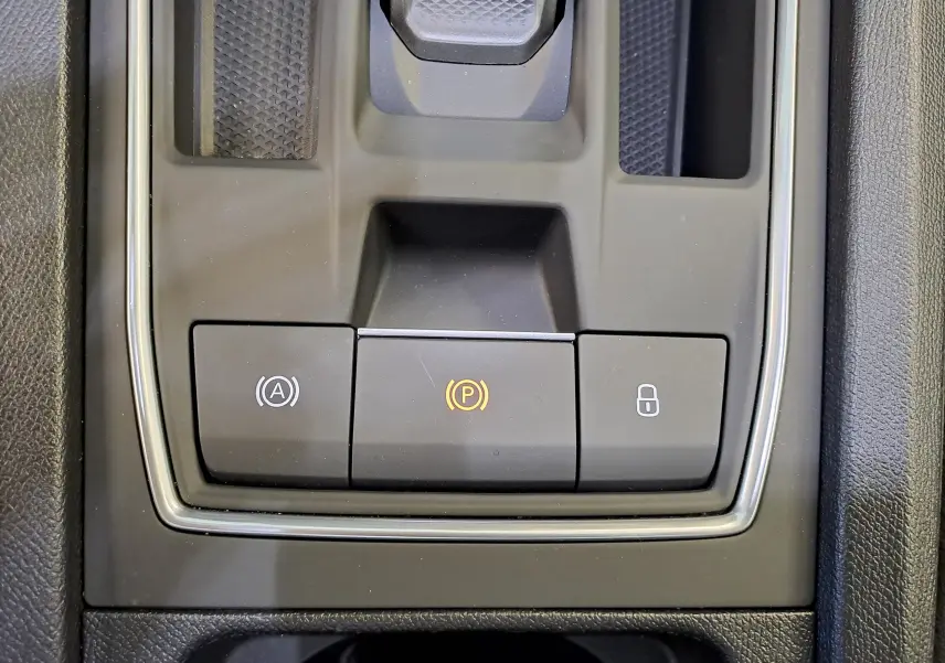 Gros plan sur la console centrale du SEAT LEON 1.5 eTSI Hybrid 2024 noir minuit, boutons de frein à main et verrouillage visibles.