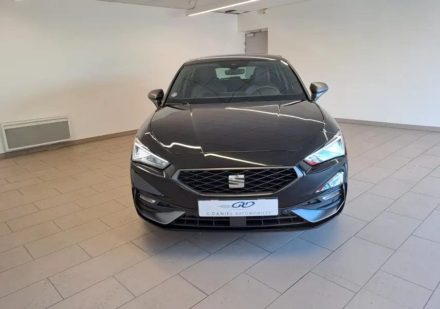 Vue frontale d'une SEAT LEON 2024 noir minuit avec phares LED allumés dans un showroom lumineux.