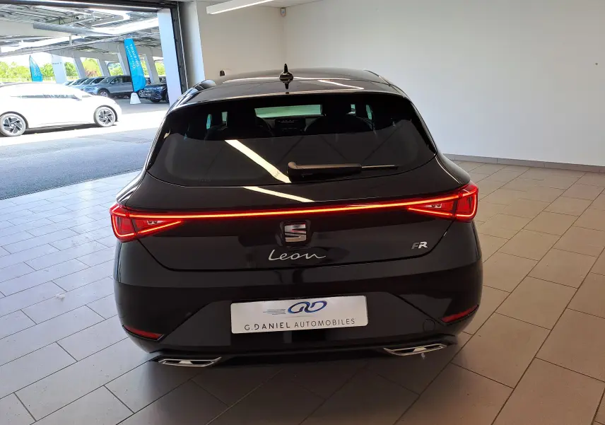 Vue arrière d'une SEAT Leon 1.5 eTSI Hybrid 150 DSG7 FR noire minuit avec feux LED continus allumés en intérieur.