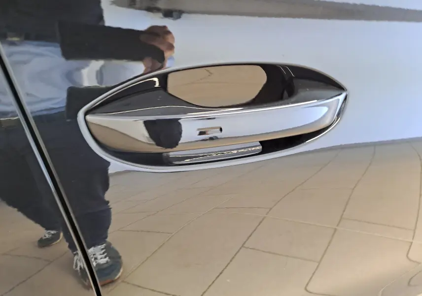 Poignée de porte chromée sur le côté gauche d'une SEAT LEON 1.5 eTSI Hybrid 2024 en noir minuit, reflet net visible.