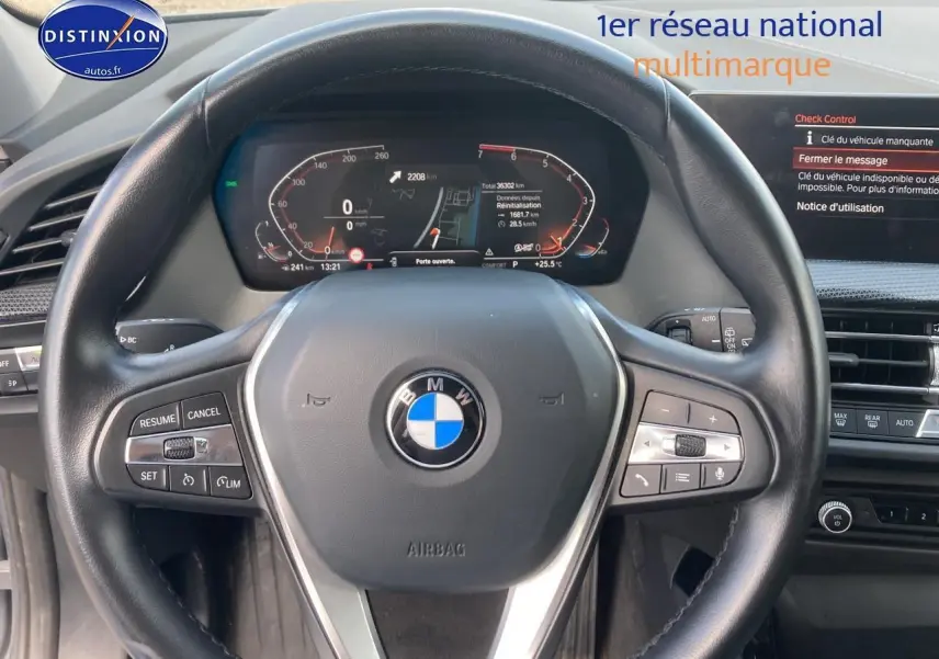 Vue rapprochée du volant cuir noir multifonction de la BMW Série 1 118i 2023 avec tableau de bord digital allumé.