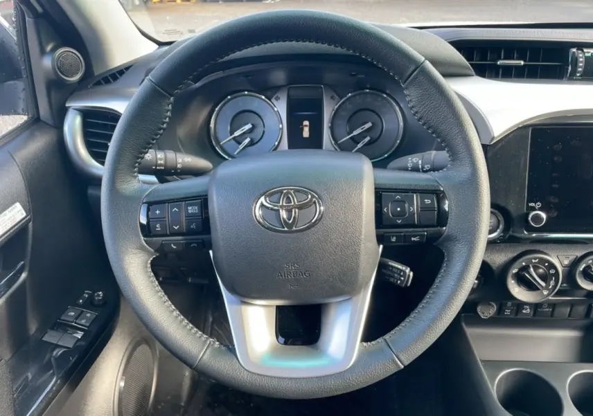 Vue intérieure centrée sur le volant cuir du Toyota Hilux 2025 avec tableau de bord et commandes visibles.