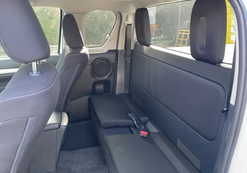 Vue intérieure arrière côté droit du Toyota Hilux 2025 blanc pur, montrant les sièges noirs et un haut-parleur intégré.