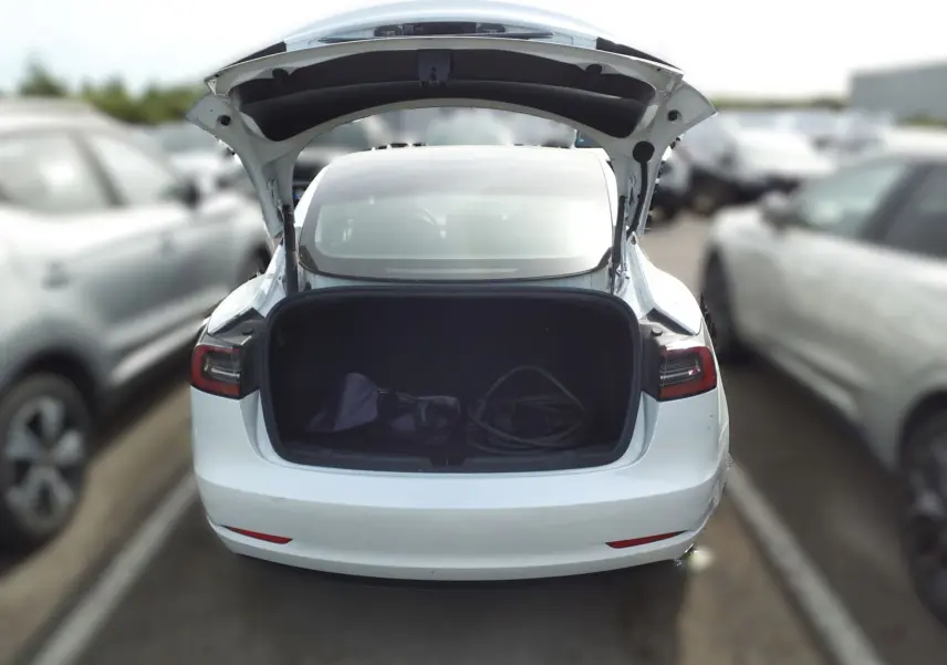 Vue arrière d'une Tesla Model 3 blanche 2023 avec coffre ouvert montrant un câble de recharge à l'intérieur.
