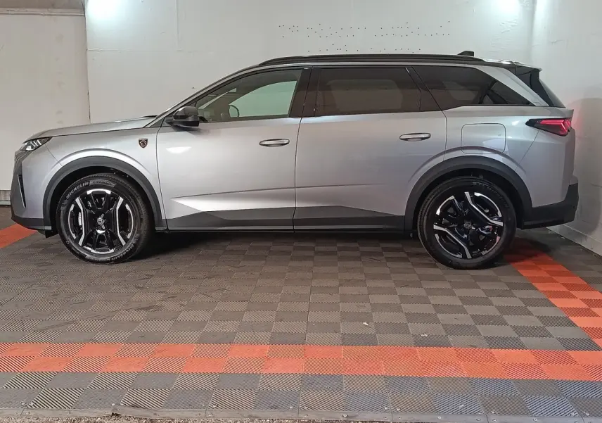Vue latérale droite d’un Peugeot 5008 gris clair avec jantes noires et toit noir en intérieur fermé.