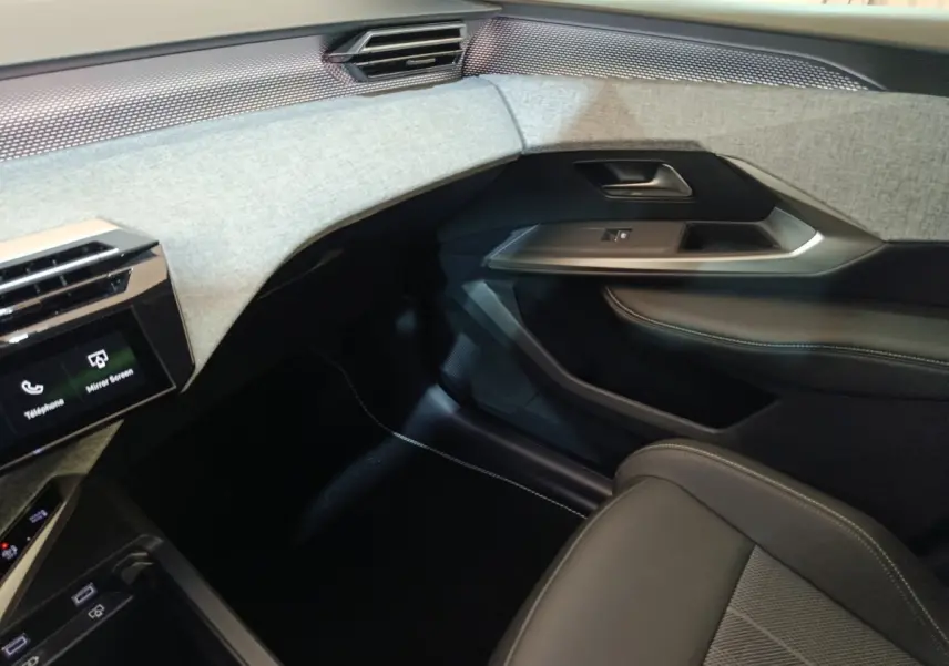 Vue intérieure côté passager du Peugeot 5008 1.6 PHEV 195 E-DCS7 GT 2026 avec tableau de bord gris clair et sièges noirs.