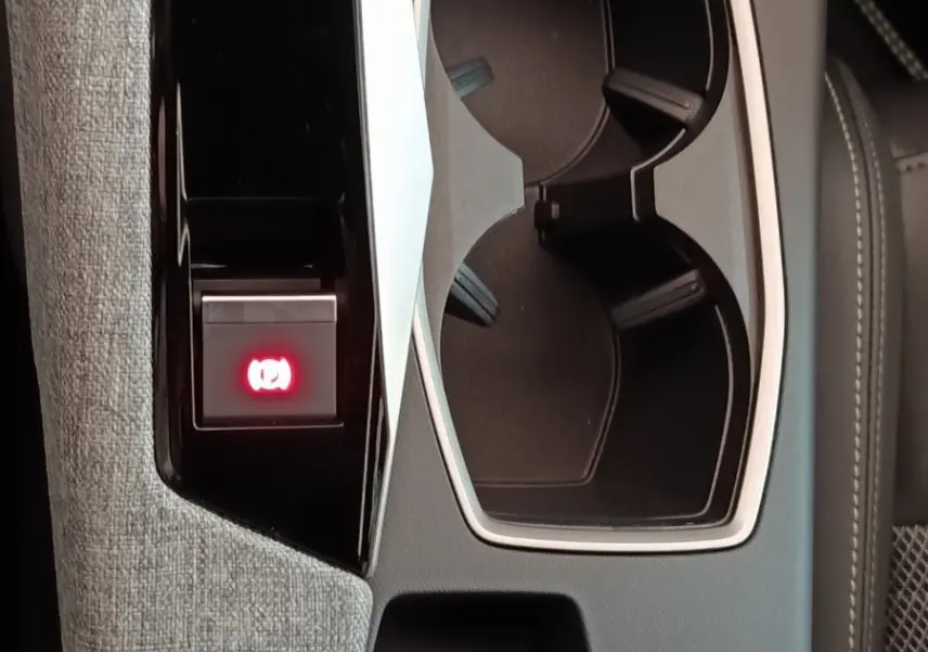 Gros plan sur la console centrale grise du Peugeot 5008 1.6 PHEV avec porte-gobelets et bouton frein à main électrique allumé.