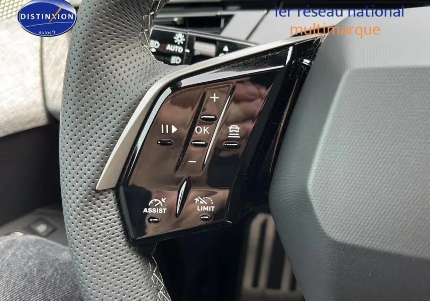 Gros plan sur les commandes multifonctions noires du volant cuir perforé côté gauche du Peugeot 3008 gris hybride 2025.