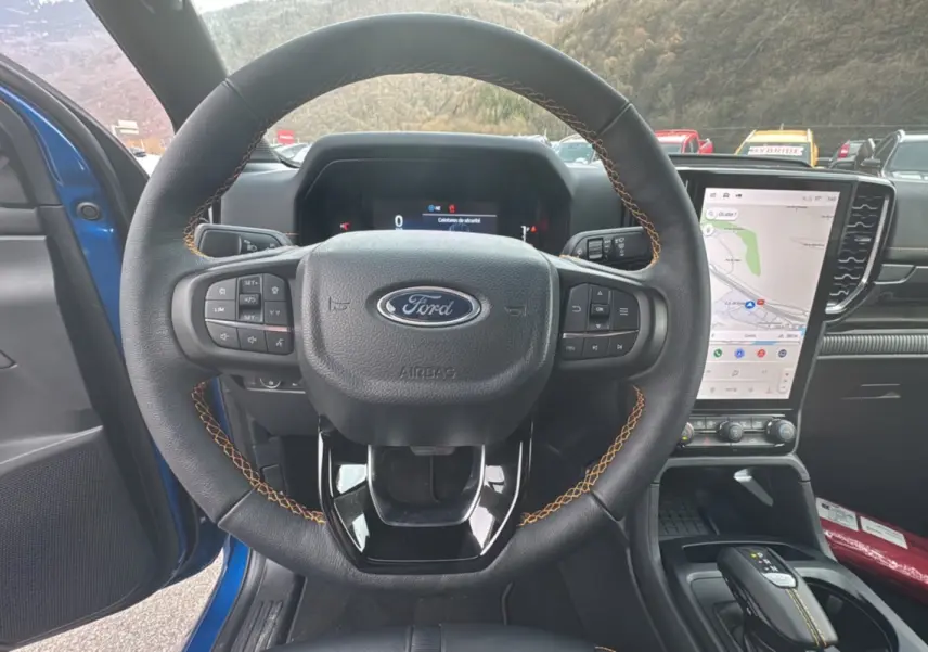 Vue centrée sur le volant cuir noir avec surpiqûres jaunes du Ford Ranger Wildtrak 2026, écran tactile vertical et intérieur bleu visible.