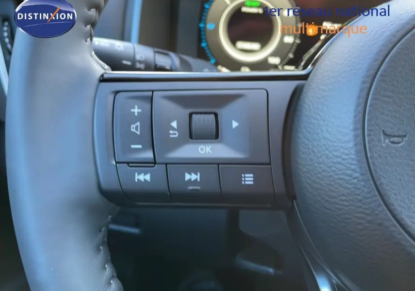 Gros plan sur les commandes gauche du volant cuir noir du Nissan Qashqai gris argile 2025, affichage numérique en arrière-plan.