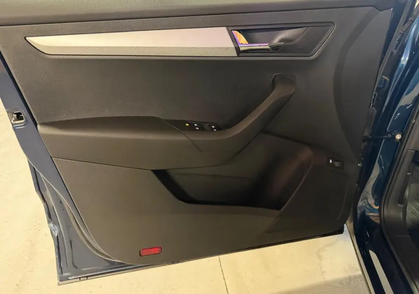 Vue intérieure de la porte avant gauche du Skoda Karoq bleu 2023 avec insert décoratif gris et poignée chromée.