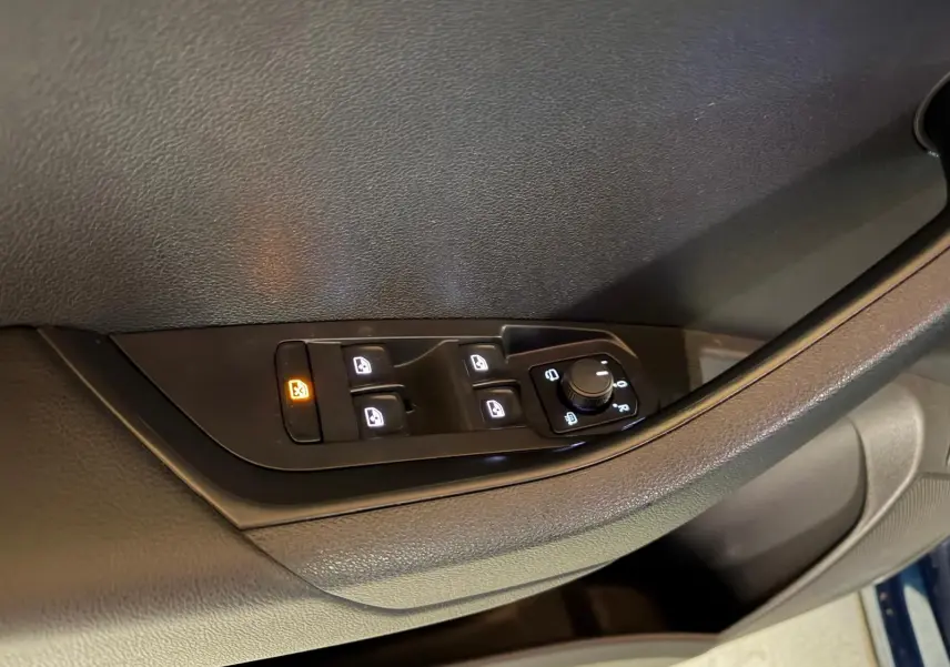 Détail de la porte côté gauche d’un Skoda Karoq bleu 2023 avec commandes de vitres et poignée chromée.