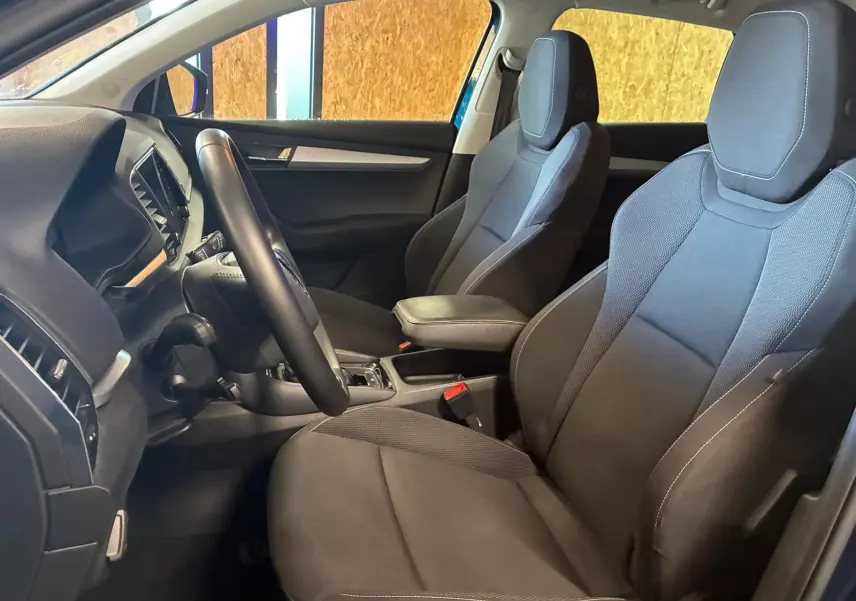 Intérieur avant du Skoda Karoq bleu 2023, sièges tissu gris foncé avec accoudoir central et volant multifonctions.