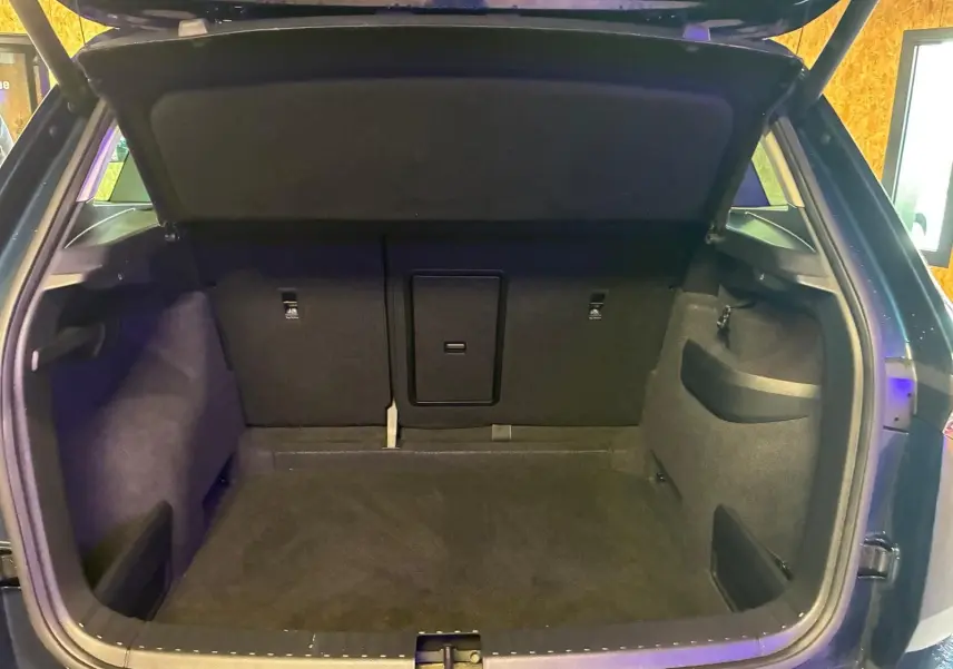 Coffre ouvert vu de l'arrière d'un Skoda Karoq bleu 2023, montrant l'espace de chargement et les rangements latéraux.