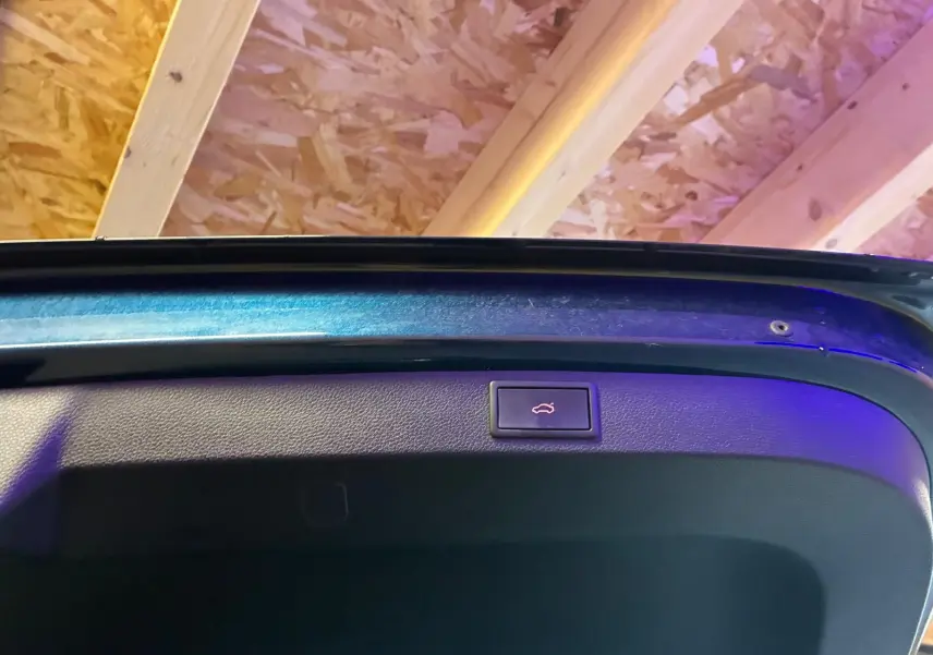 Bouton d'ouverture électrique du hayon sur la face intérieure d'un SKODA KAROQ bleu, vue rapprochée du coffre ouvert.