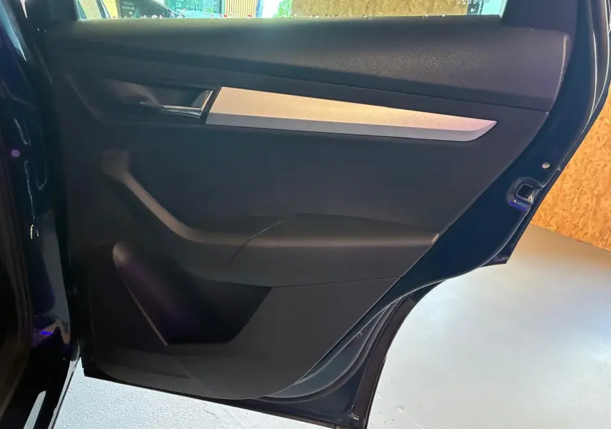 Vue rapprochée de la porte arrière gauche bleu foncé d'un Skoda Karoq 2023 avec insert décoratif gris et poignée chromée.