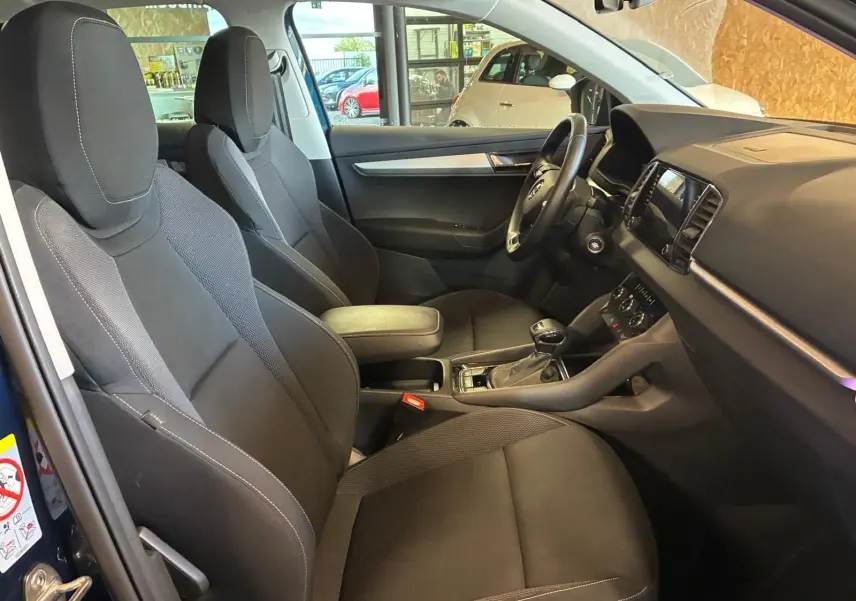 Vue intérieure côté gauche du Skoda Karoq bleu 2023, montrant les sièges avant noirs et le tableau de bord.