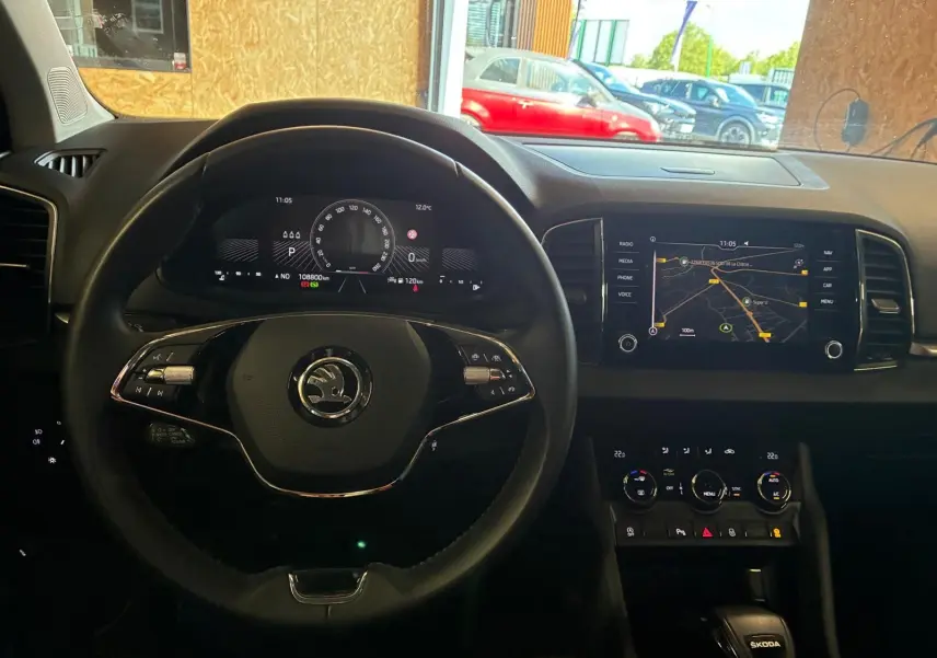 Vue intérieure centrée sur le volant multifonctions et le tableau de bord numérique d'une Skoda Karoq 2023, avec écran tactile de navigation.