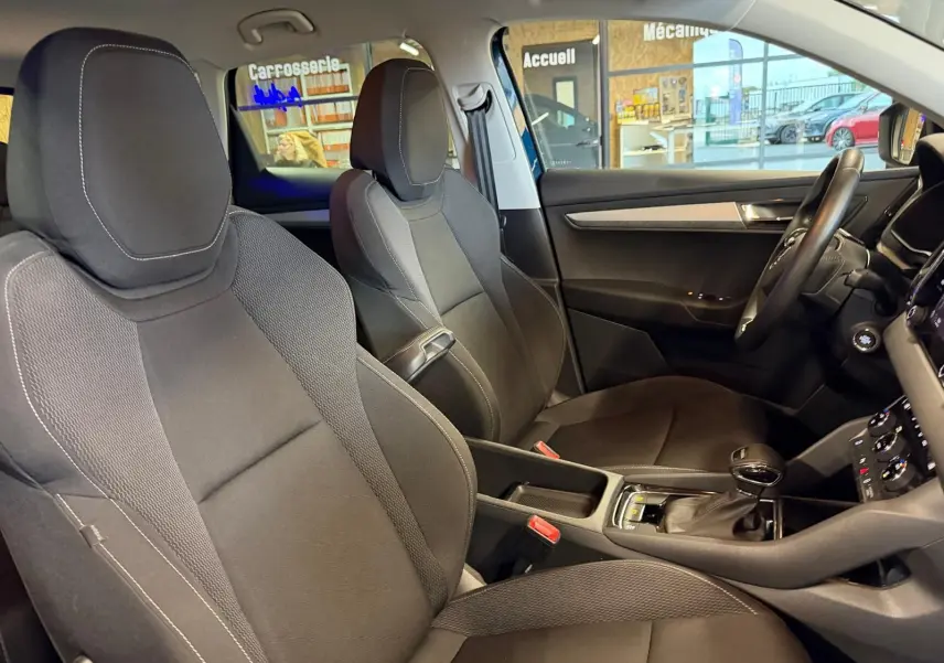 Vue plongeante sur la console centrale noire avec levier de vitesse automatique et sièges tissu noir du Skoda Karoq bleu 2023.