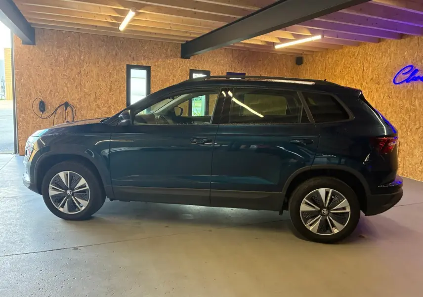Vue de profil côté gauche d'un SKODA KAROQ bleu 2023 avec jantes alu 17 pouces dans un garage.