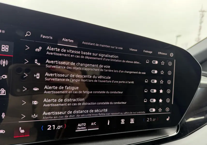 Audi Q6 e-tron gris nacré en vue 3/4 avant, avec jantes noires sport à 5 branches en Y et étriers rouges visibles.