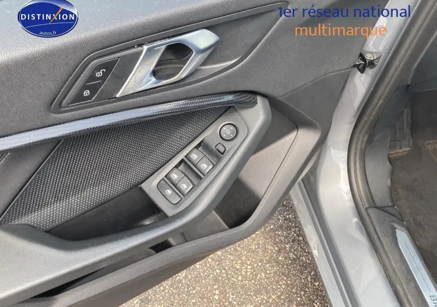 Détail de la porte avant gauche grise d'une BMW Série 1 118i 2023 avec commandes des vitres et serrure intégrée.