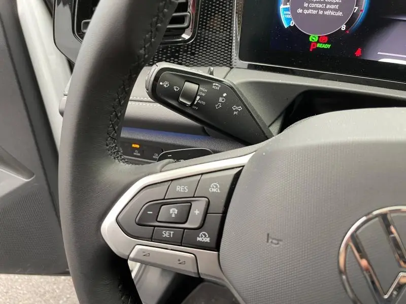 Gros plan sur le volant cuir noir côté gauche du Volkswagen Tiguan blanc, avec commandes de régulateur et commodo d’essuie-glace.